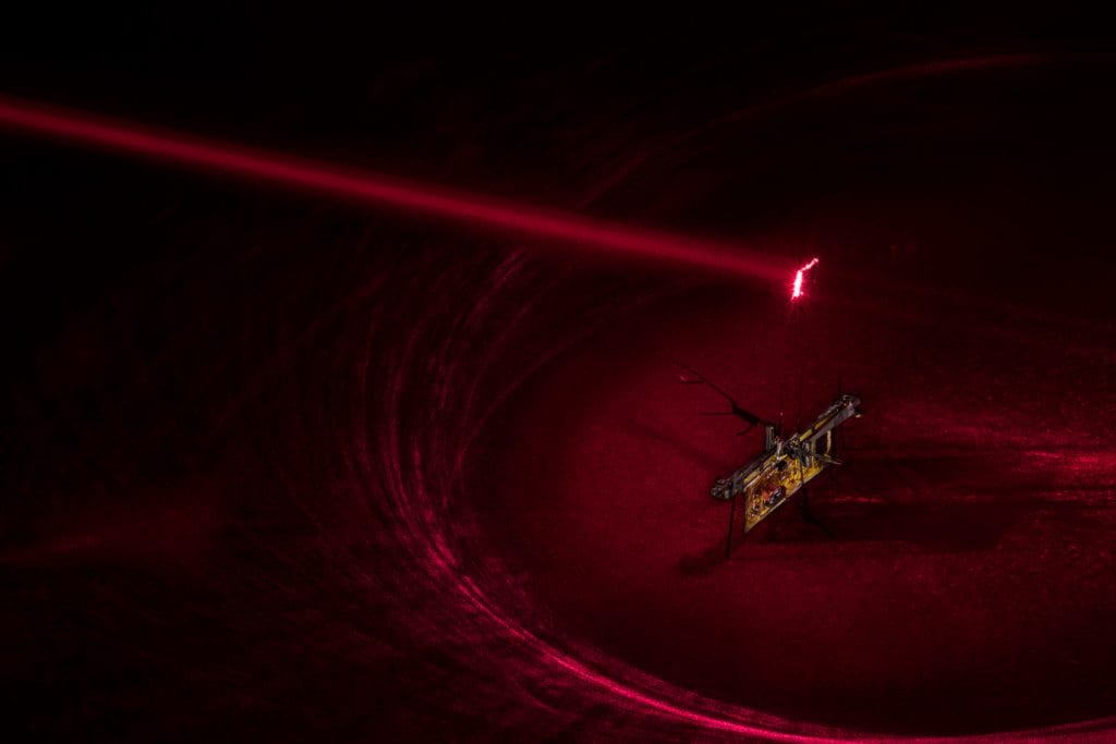 To power RoboFly, the engineers pointed an invisible laser beam (shown here in red laser) at a photovoltaic cell, which is attached above the robot and converts the laser light into electricity.Mark Stone/University of Washington