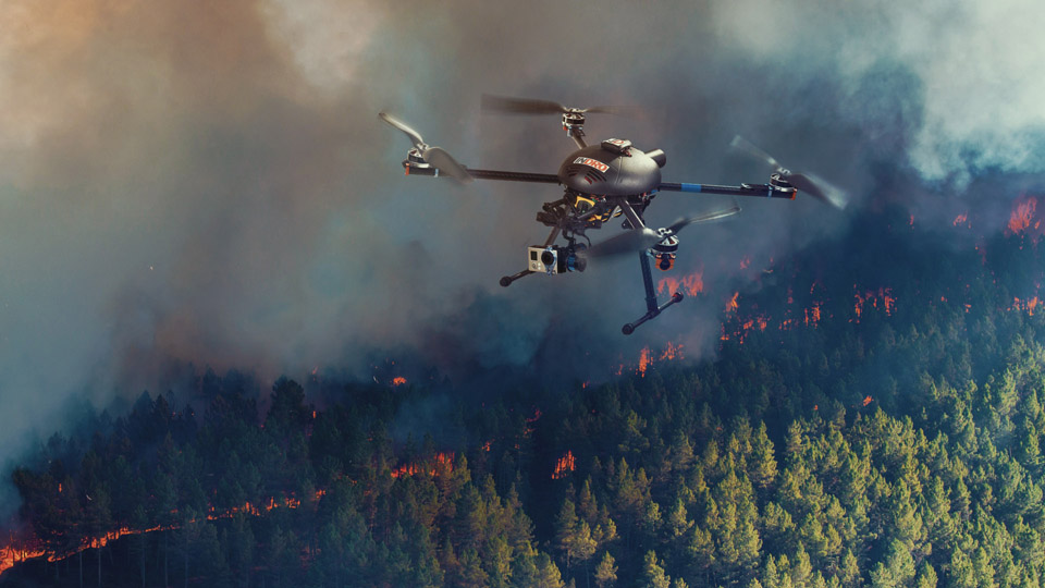A small UAV is shown surveying the movement of a forest fire. The EOAMS would allow first responders to deploy drones at disaster scenes without endangering other emergency response aircraft or commercial flights. [photo illustration by Kongsberg Geospatial]