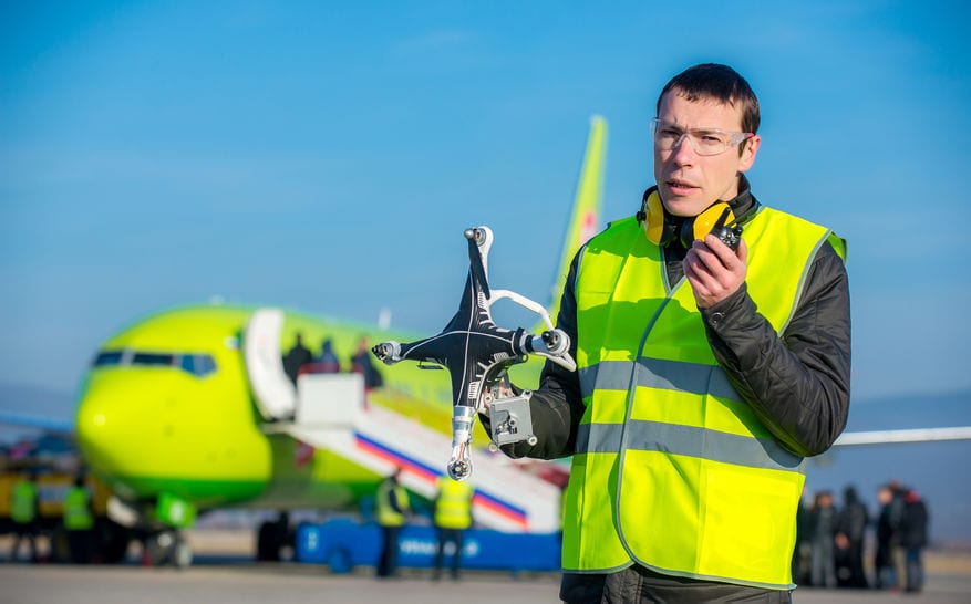 An airport worker holding crashed quadcopter near airliner | Mark Agnor