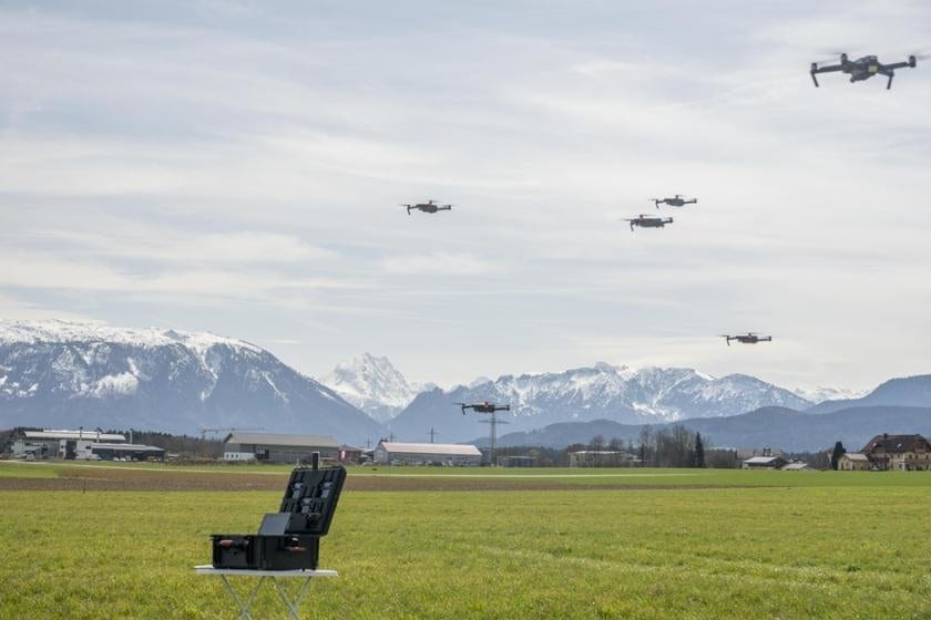 Photogrammetry Swarm in action, with five MP drones in swarm formation hovering above the transport container during a test flight in 2018; a sixth drone is filming the swarm.